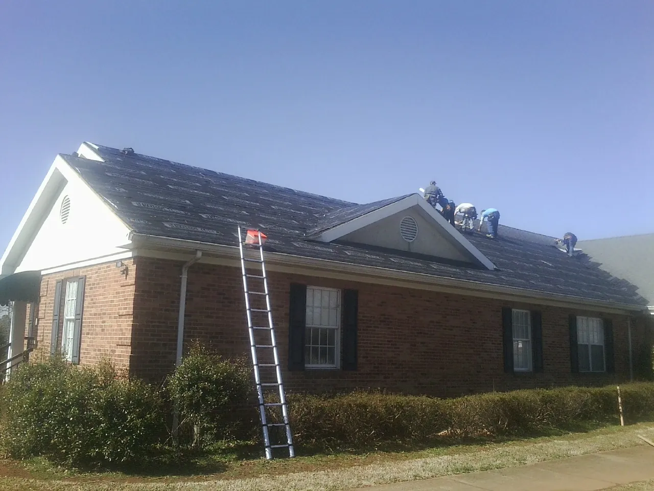 Crew tearing shingles off a brick ranch roof with a ladder set — Metal Roof Repair work by our crew in Aurora